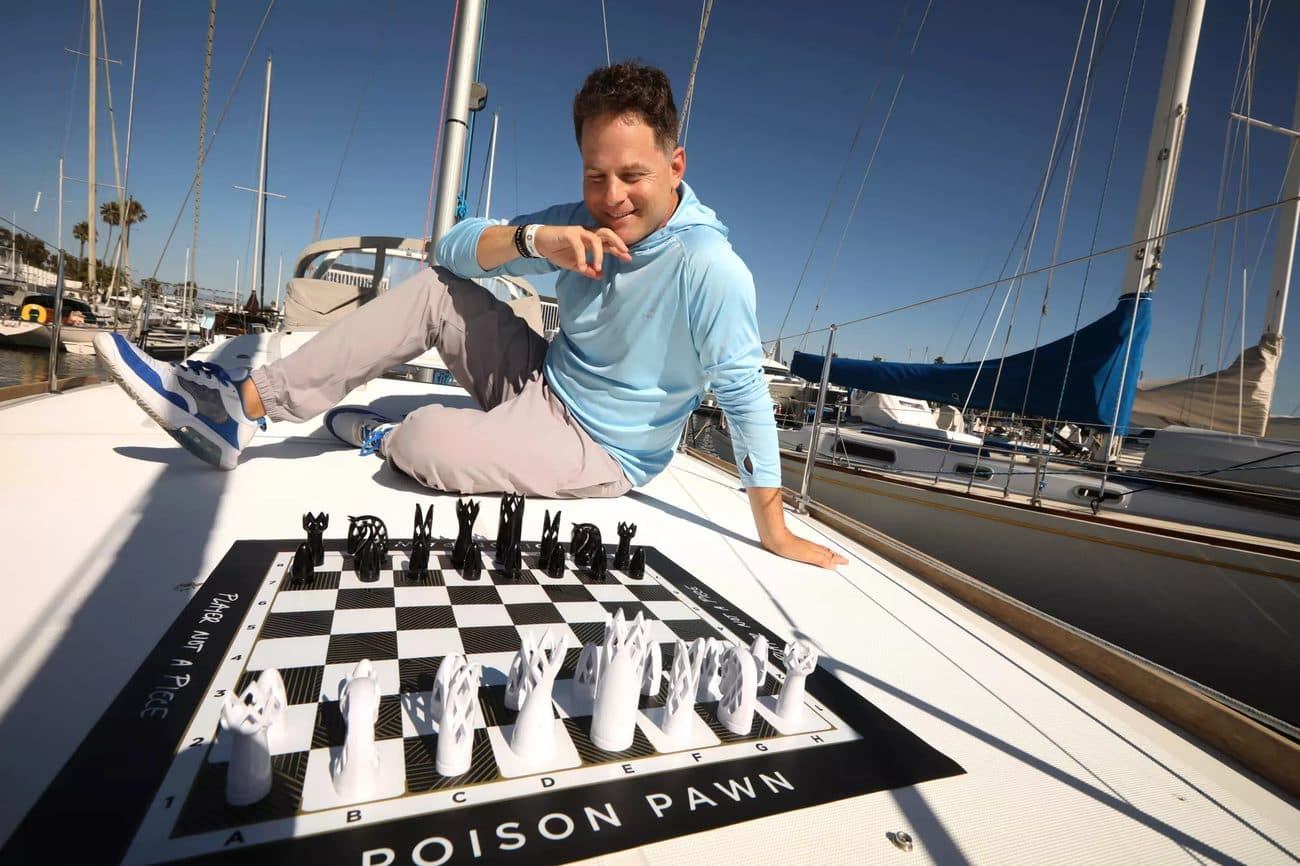 Seth Makowsky sits on the deck of a sailboat in Marina del Rey with a Poison Pawn chess set laid out in front of him.
